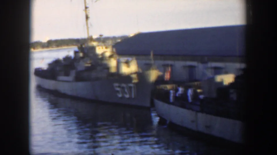 1951 Cuba home-movie frame showing a gray U.S. Navy destroyer marked 537 moored beside a pier, with crew figures on deck and harbor water below.
