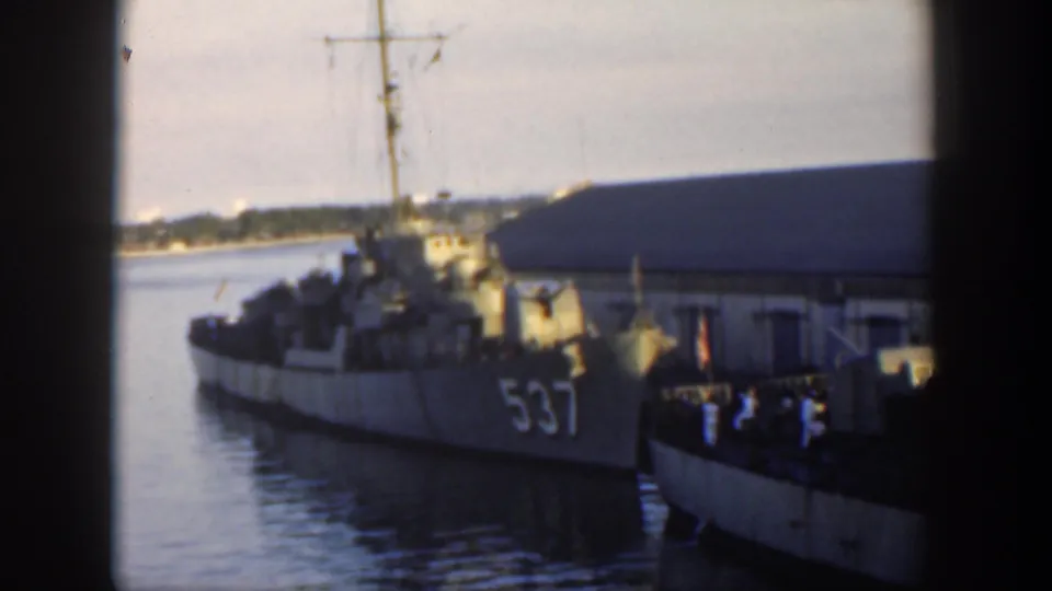 1951 Cuba frame of the U.S. Navy destroyer marked 537 at dock, with mast rigging, crew shapes, a pier building, and shoreline in the background.