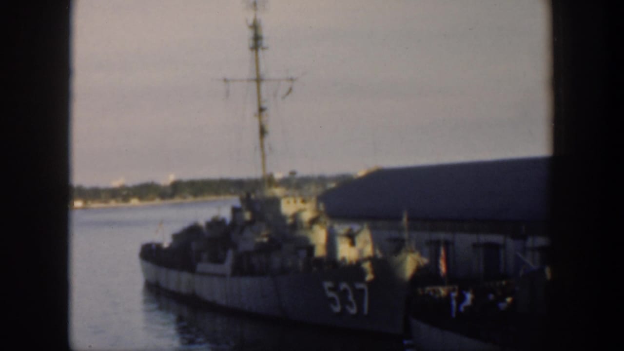 1951 Cuba home-movie frame showing a docked naval vessel marked 537 beside a waterfront building, viewed through a window.