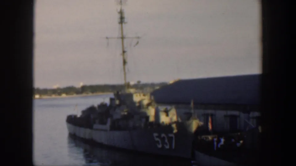 1951 Cuba home-movie frame showing a docked naval vessel marked 537 beside a waterfront building, viewed through a window.