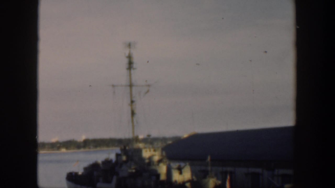 Naval ship and waterfront building partly obscured by a vertical window bar.
