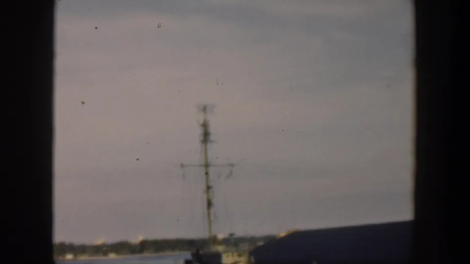 1951 Cuba home-movie frame emphasizing the ship mast, low waterfront building, harbor water, and distant shoreline.