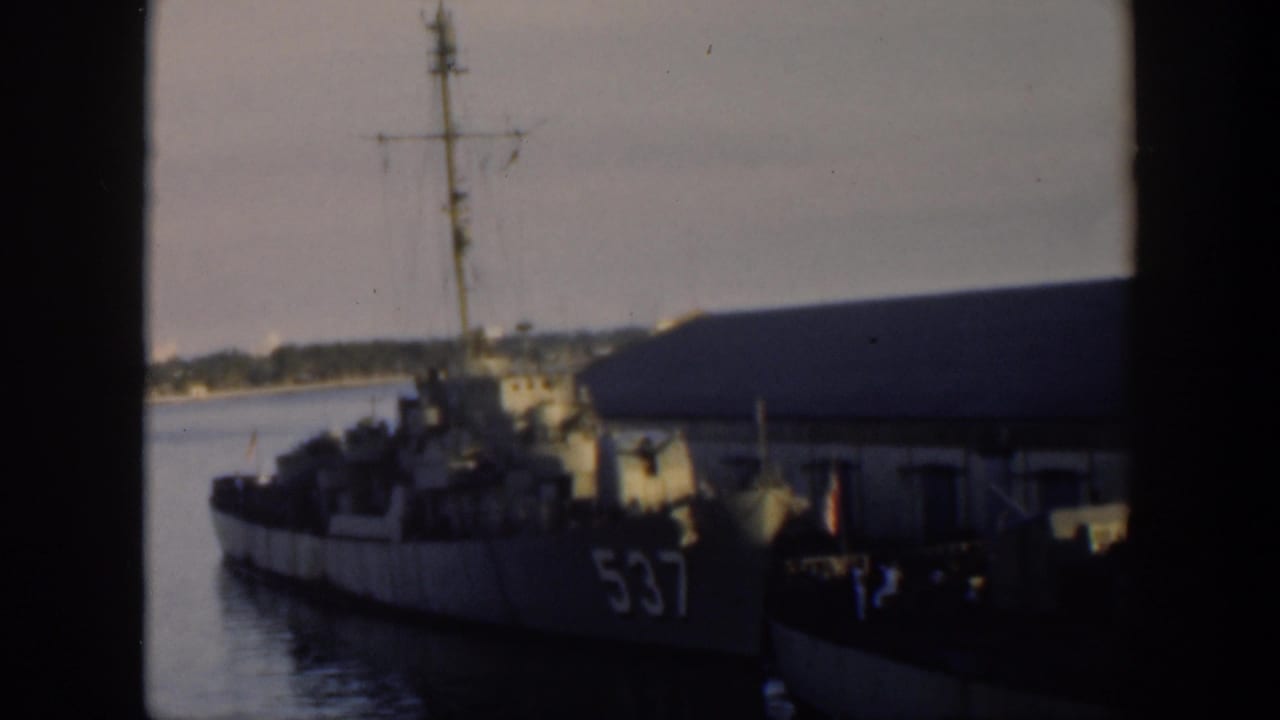 Naval vessel with hull number 537 docked beside a low waterfront building.