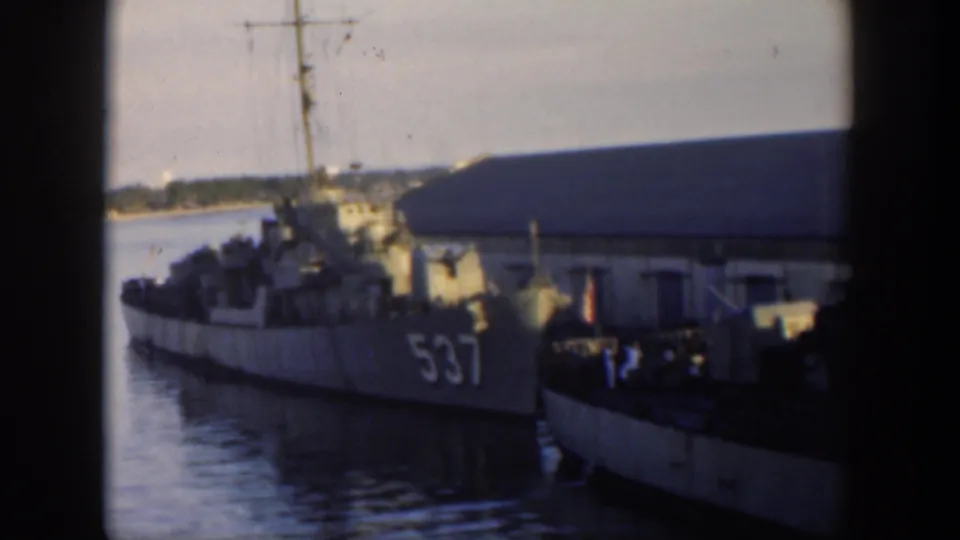1951 Cuba home-movie view of naval vessel 537 moored near a pier, partly blocked by a dark foreground boat and frame edge.