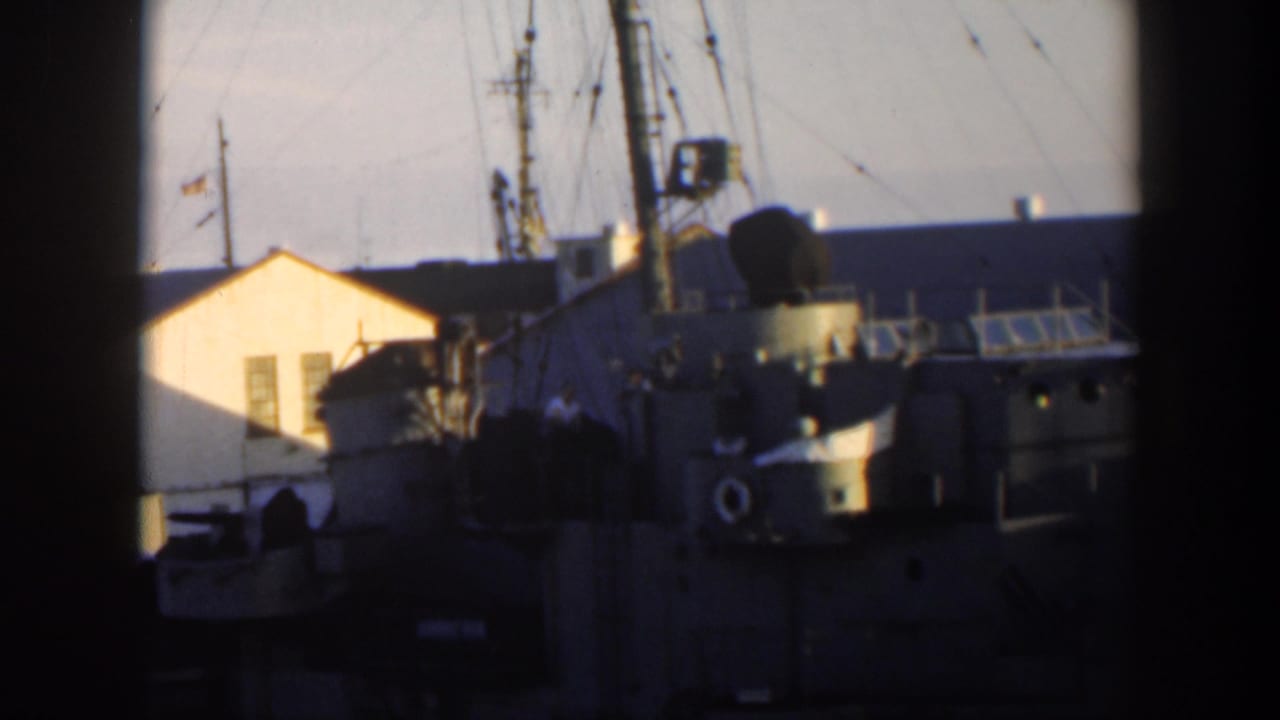 Naval ship at a dock beside a yellow building, seen through dark frame edges.