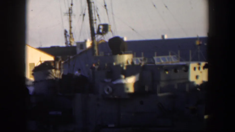 1951 Cuba home-movie view of a docked naval vessel with portholes, railing lines, rigging, and shadowed waterfront structures.
