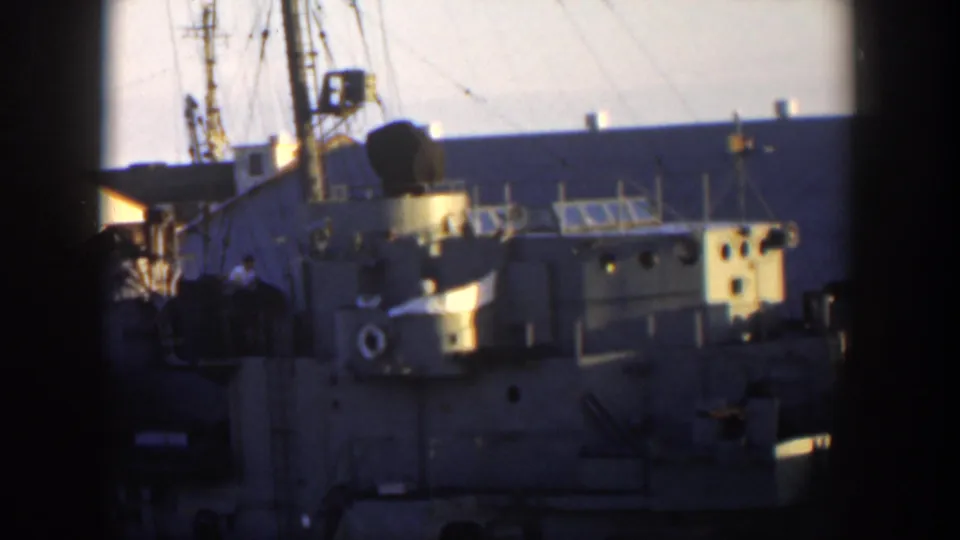 1951 Cuba frame showing a gray naval ship at dock with railings, portholes, a life ring, and indistinct people near the vessel.