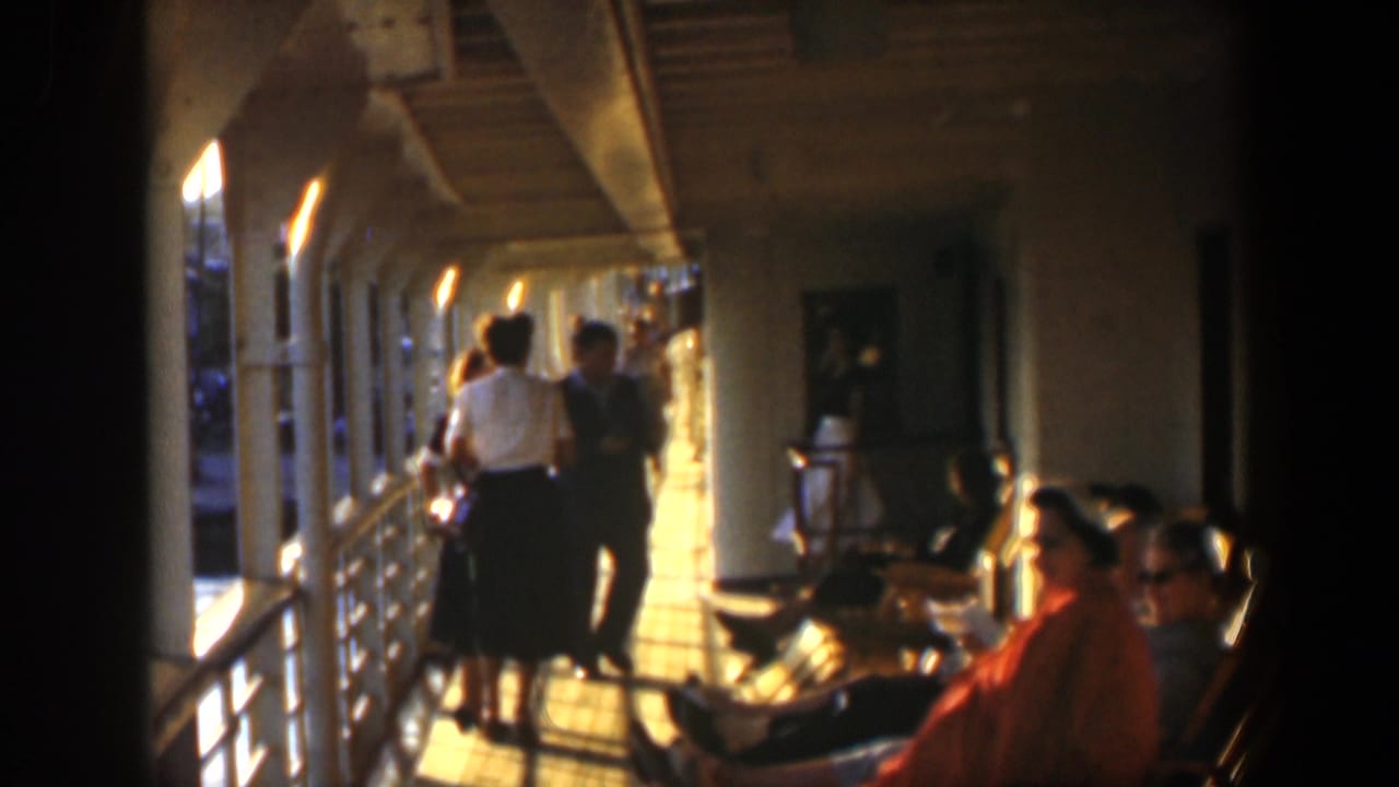People sit and walk in a sunlit corridor with benches and metal railings.
