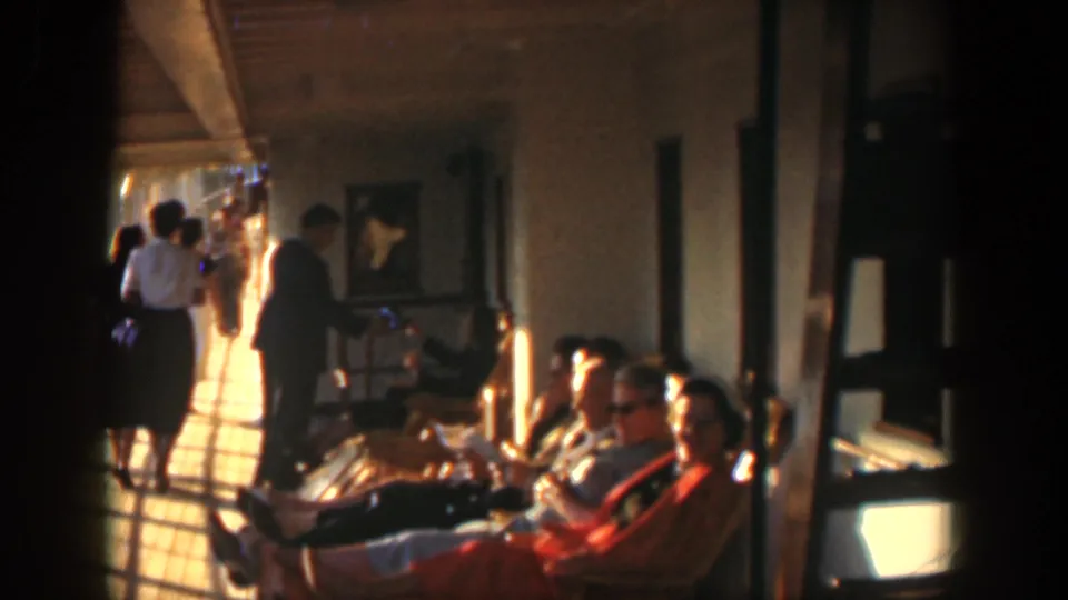 1951 Cuba 8mm still of adults seated near the camera while others continue down a hospital or clinic corridor.