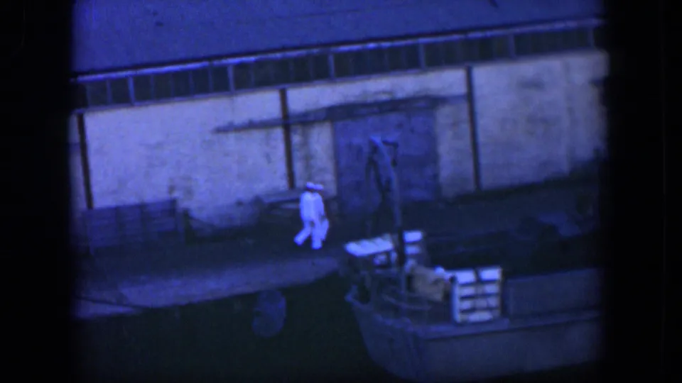 Cuba 1951 frame with sailors in white uniforms moving past crates near a docked boat and waterfront building.