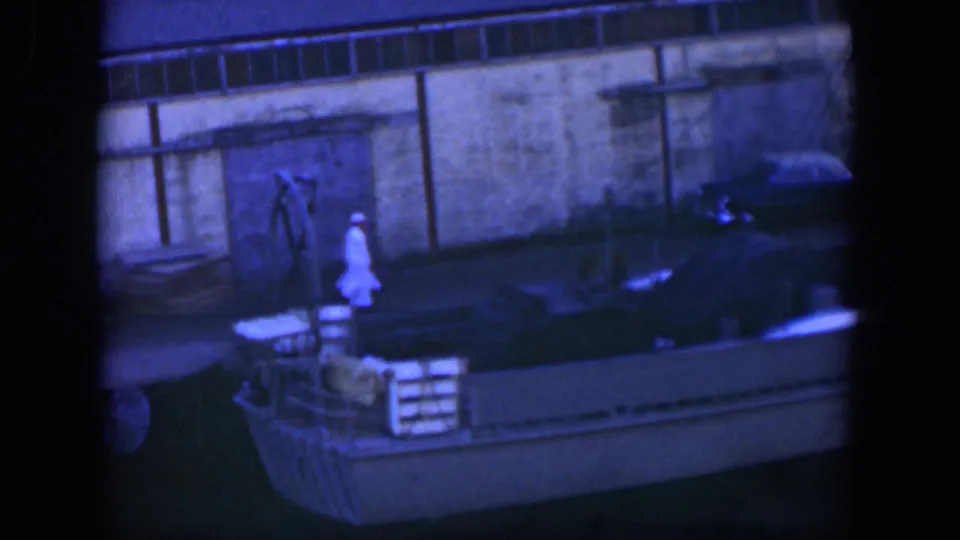 In Cuba 1951 home-movie footage, a man in white walks along a dock beside a moored boat, with a wall and parked car behind him.