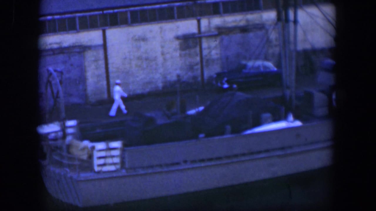 Man in white walks along the dock near a moored boat and parked car.