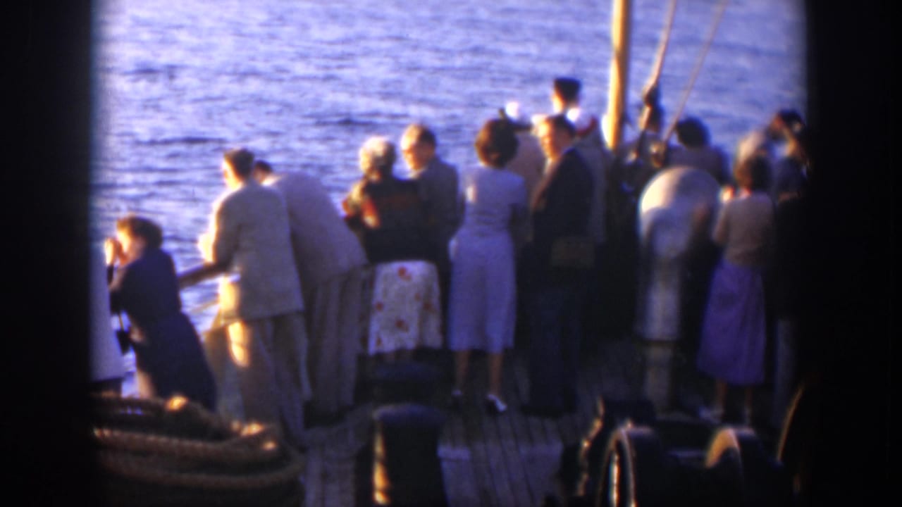 Passengers stand along a boat railing looking out over blue water.