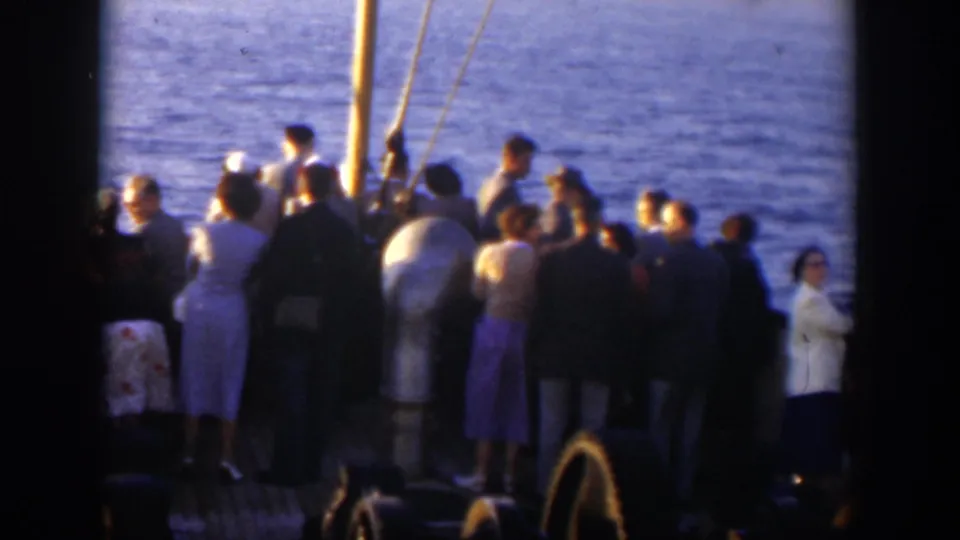A crowded boat deck in Cuba shows passengers in dresses, suits, and hats facing the water during the ride.