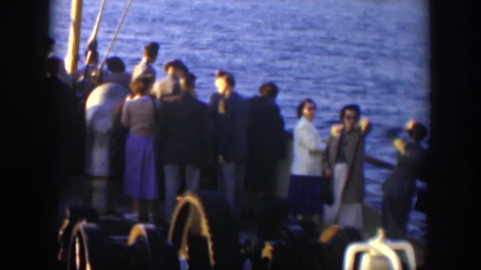 Formally dressed passengers aboard a Cuba boat ride stand near the rail as sunlight catches the water behind them.