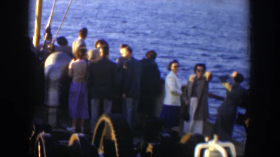 In 1951 Cuba-related 8mm footage, adult ship passengers in coats, suits, and skirts gather by the rail and look toward the sea.