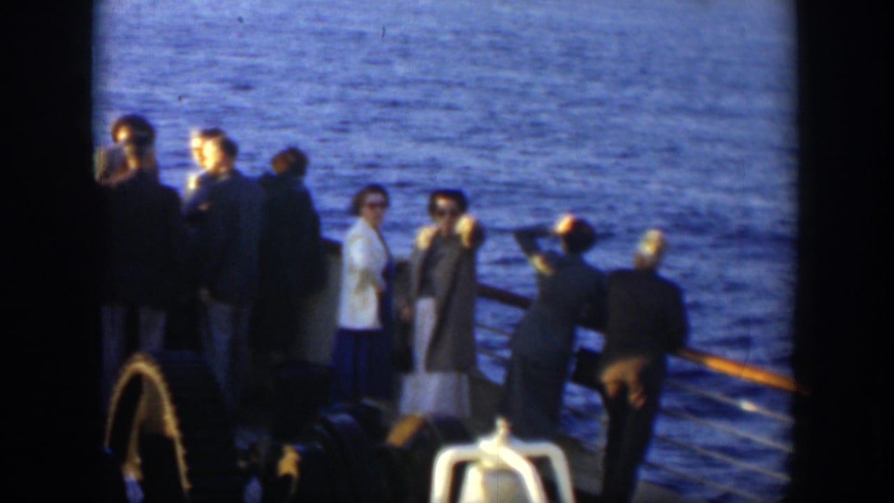 Passengers on a ship deck look outward beside the railing and ocean.