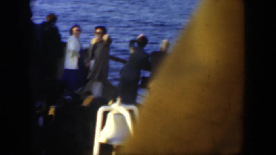 A handheld 8mm frame partly obscures the deck as adult passengers remain near the rail, with the ocean visible behind them.