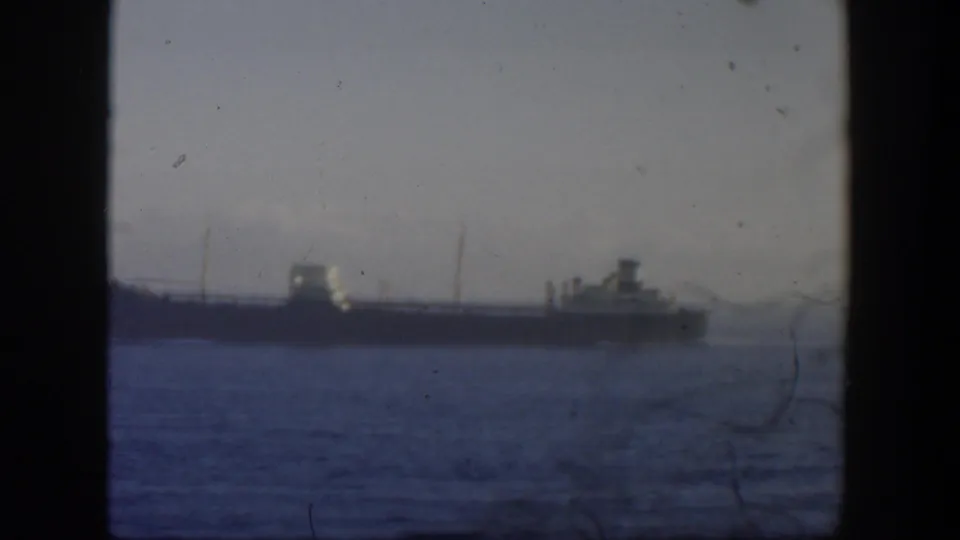 1951 Cuba-area 8mm frame with a distant cargo vessel, calm water, and a faint hazy background shape.