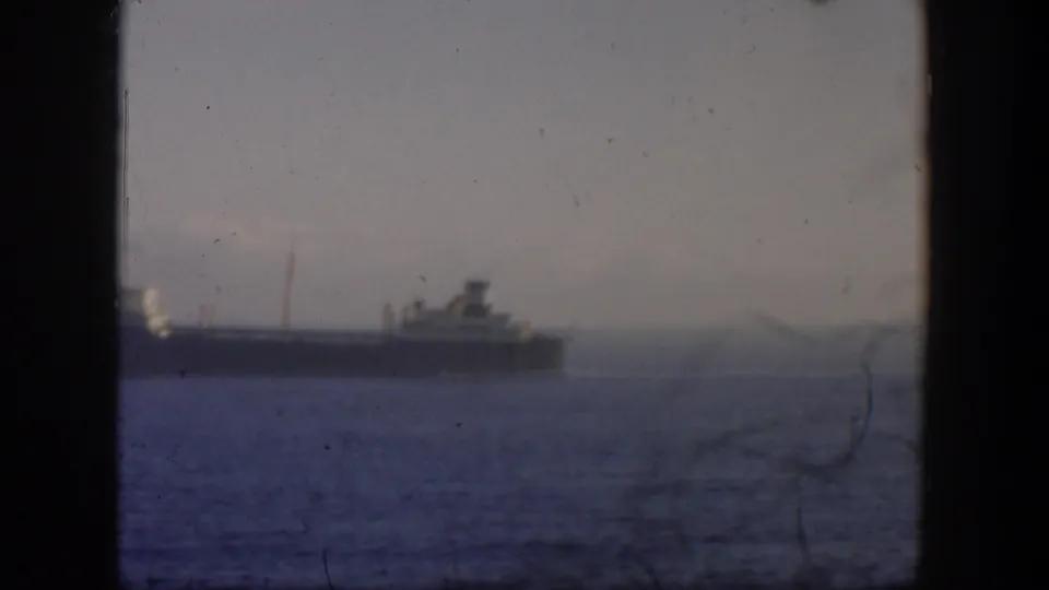 1951 Cuba home-movie frame showing a distant ship on the water, with haze, soft focus, and a dark vertical window frame.