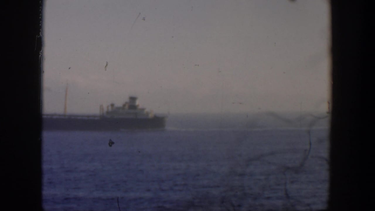 Ship on the horizon viewed through a window, with water in the foreground and haze behind it.