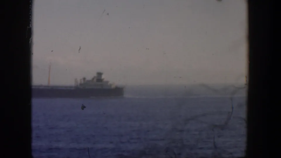 Distant ship off Cuba in 1951, framed by dark window edges with muted color, water, and a hazy shoreline atmosphere.