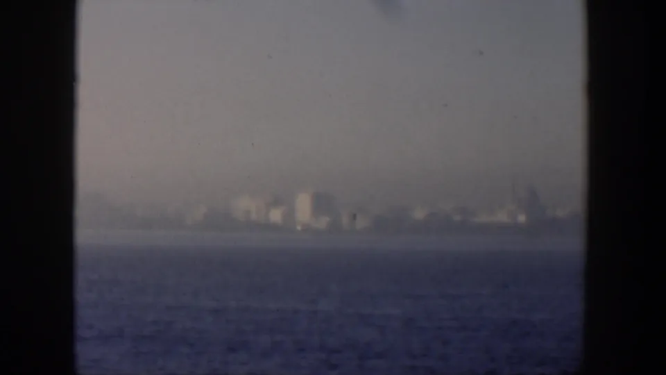 1951 Cuba frame with distant waterfront buildings across blue water, seen through a windowed home-movie view.