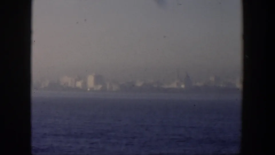Hazy 1951 Cuba waterfront view with low distant buildings, open water, and dark framing from a window or interior edge.