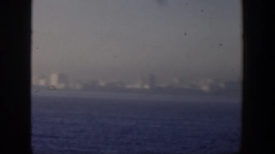 Hazy Cuban coastal skyline across blue water, partly divided by dark foreground framing in a 1951 8mm home-movie shot.