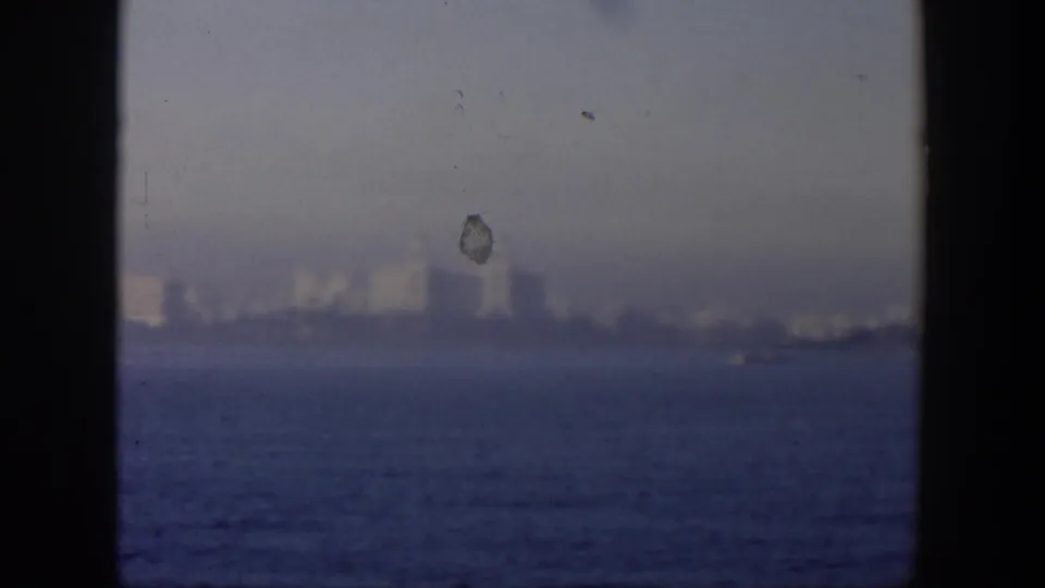 Distant Cuban shoreline and blue ocean in a hazy 1951 8mm frame, with dark foreground edges and a visible film mark.