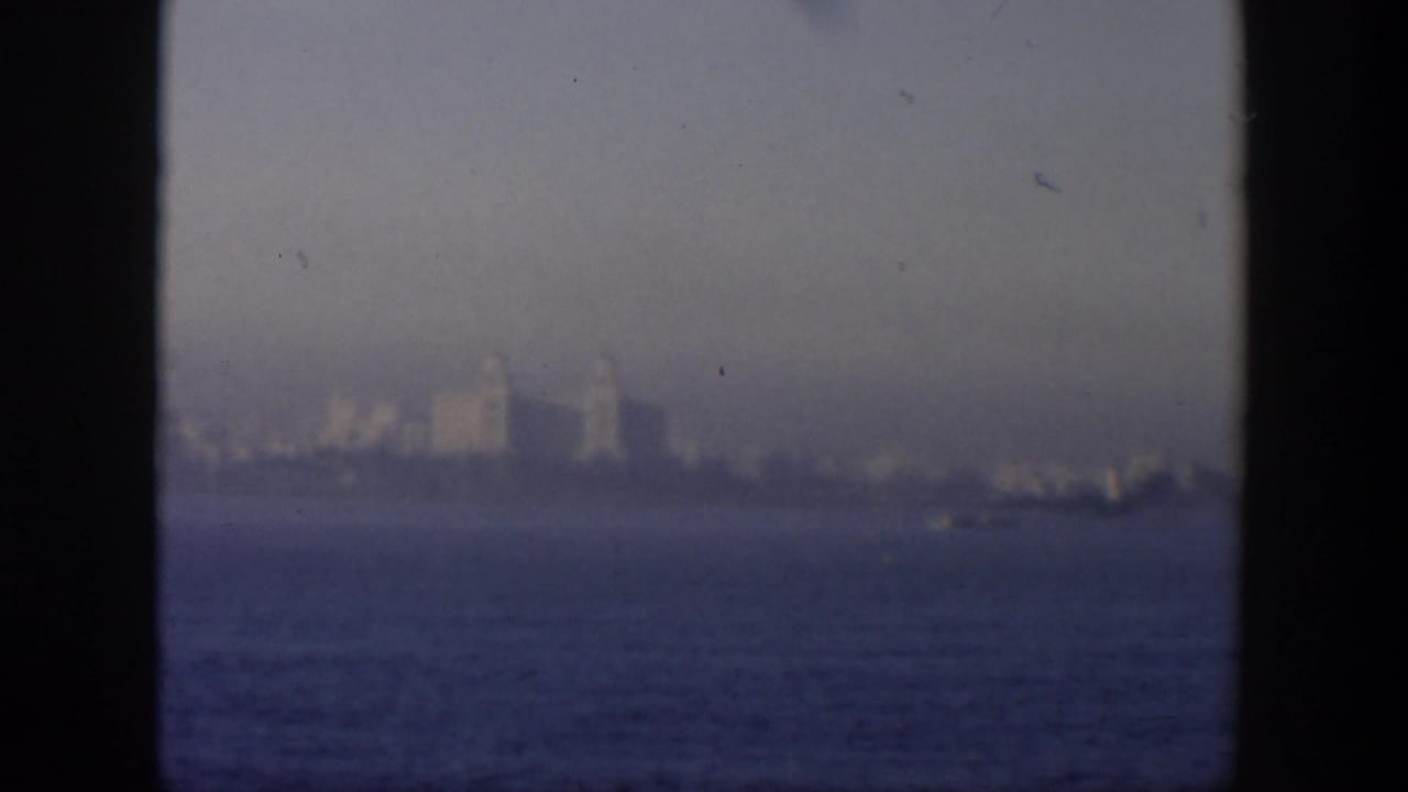 Distant waterfront skyline seen across water through haze and film grain.
