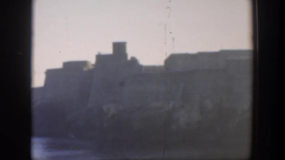 1951 Cuba coastal building silhouette viewed across water, with grain and dark 8mm frame edges.