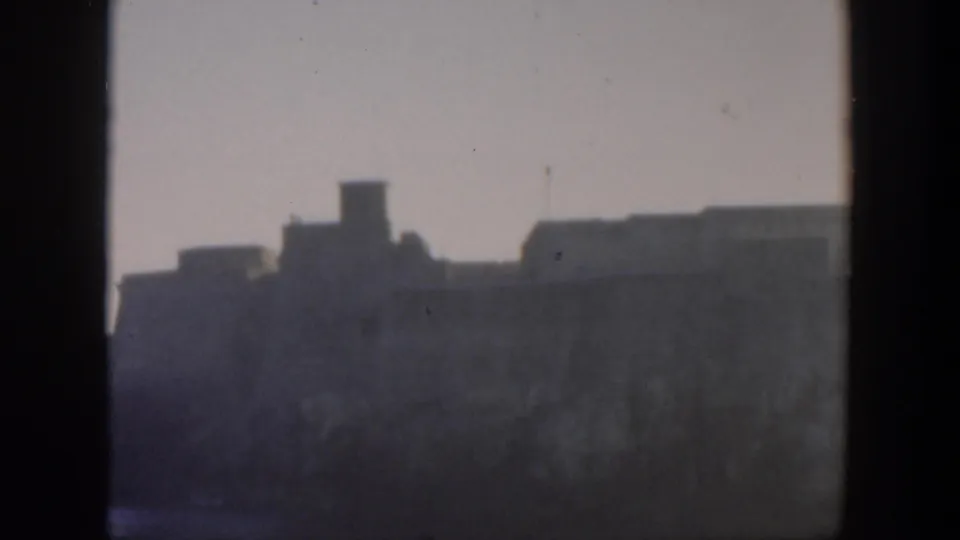 1951 Cuba 8mm frame showing a hazy distant coastal fortress or stone structure partly blocked by dark window framing.