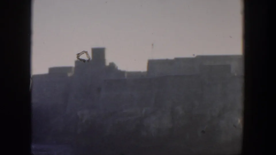 1951 Cuba frame with a distant coastal structure under pale haze, divided by a dark foreground bar.