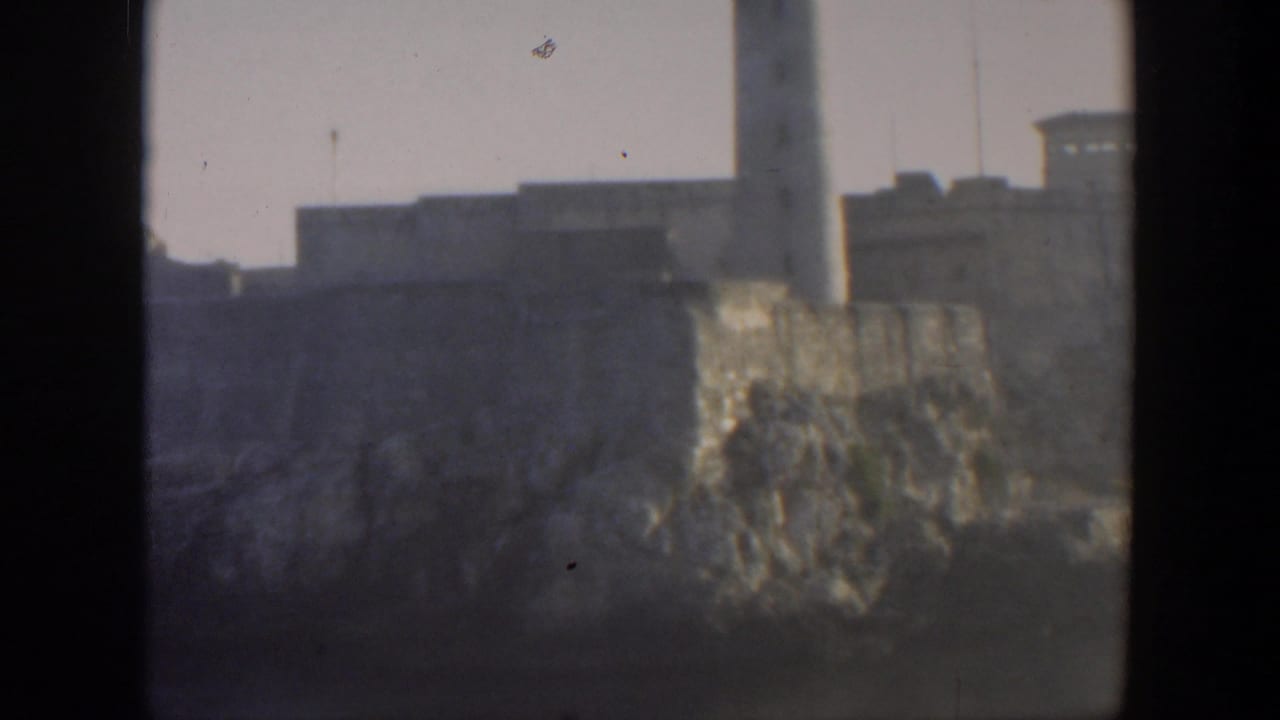 Distant lighthouse and stone coastal fortress above rocky shoreline.