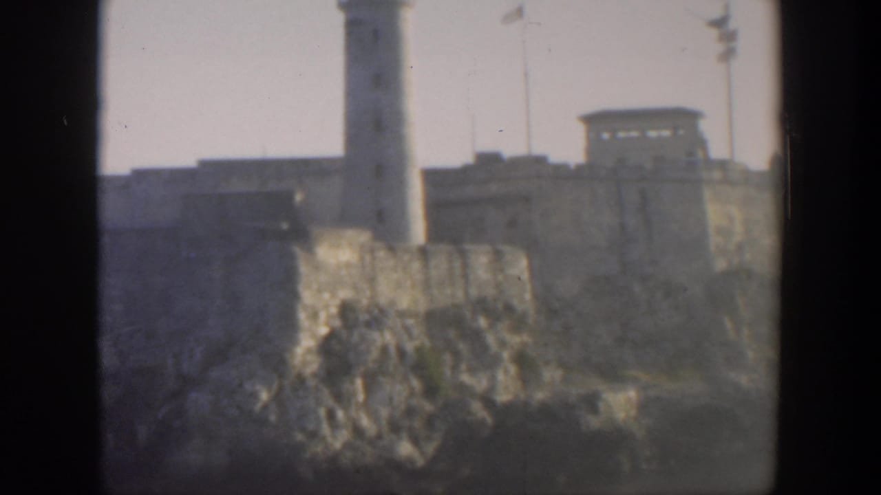 Coastal fortress wall with lighthouse tower and small flags in the distance.