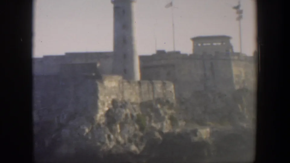 1951 Cuba frame with the lighthouse partly centered over rugged rock and fortress walls, seen through dark film-frame borders.