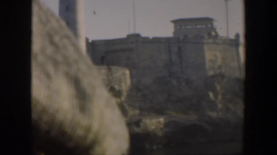 1951 Cuba 8mm frame showing a fortified wall and lookout structure, with the lighthouse partially visible near the left edge.