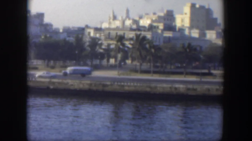 1951 Cuba 8mm frame showing a white bus and period cars on a coastal road beside blue water.