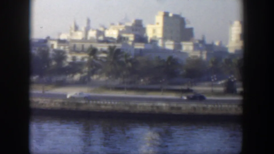 1951 Cuba urban waterfront view with cars on the road, palms, pale buildings, and a tower-like structure in the distance.