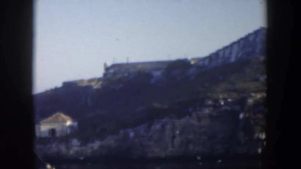 1951 Cuba coastal hillside view with water below, rocky slope, a small structure, and a larger building on the ridge.