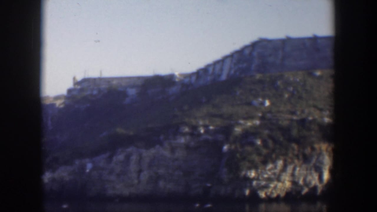 Cliffside structure seen from a distance with dark vertical film borders.