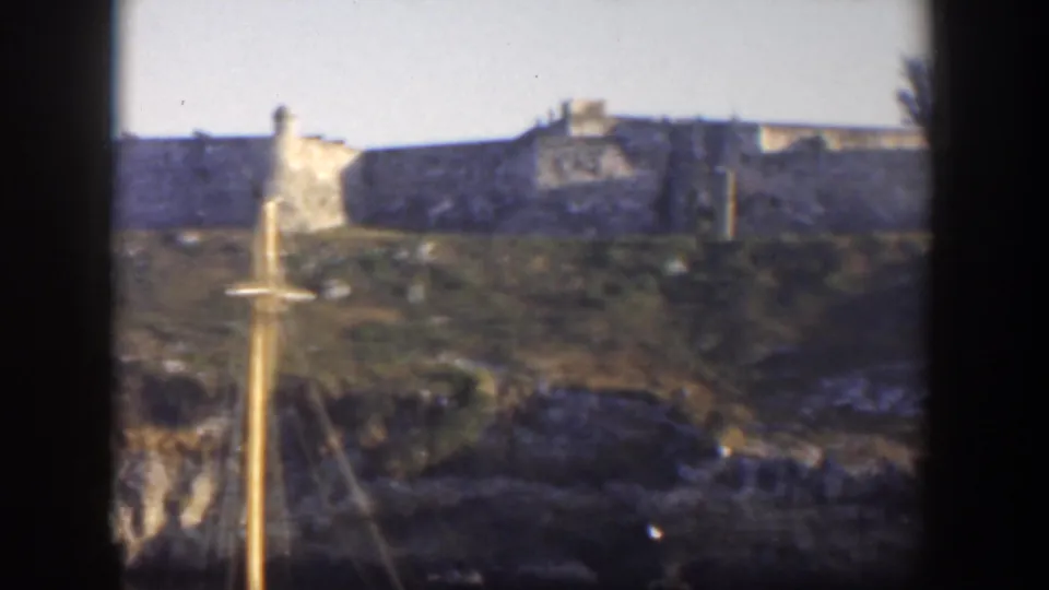 1951 Cuba 8mm frame with hillside fort walls, a small tower, and a sailboat mast cutting through the foreground.