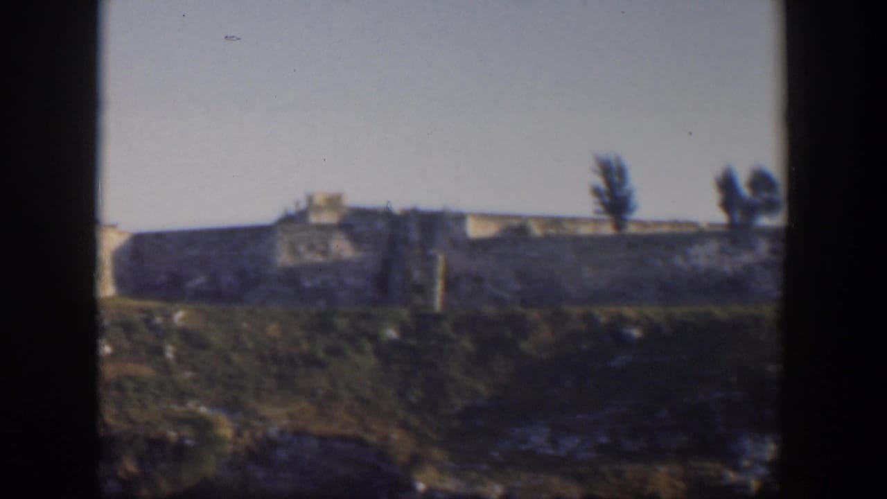Small white building above a low shoreline, seen through dark film edges.