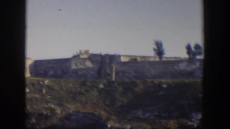 1951 Cuba 8mm frame showing a small white building or wall near a shoreline, with dark film-gate borders and soft focus.