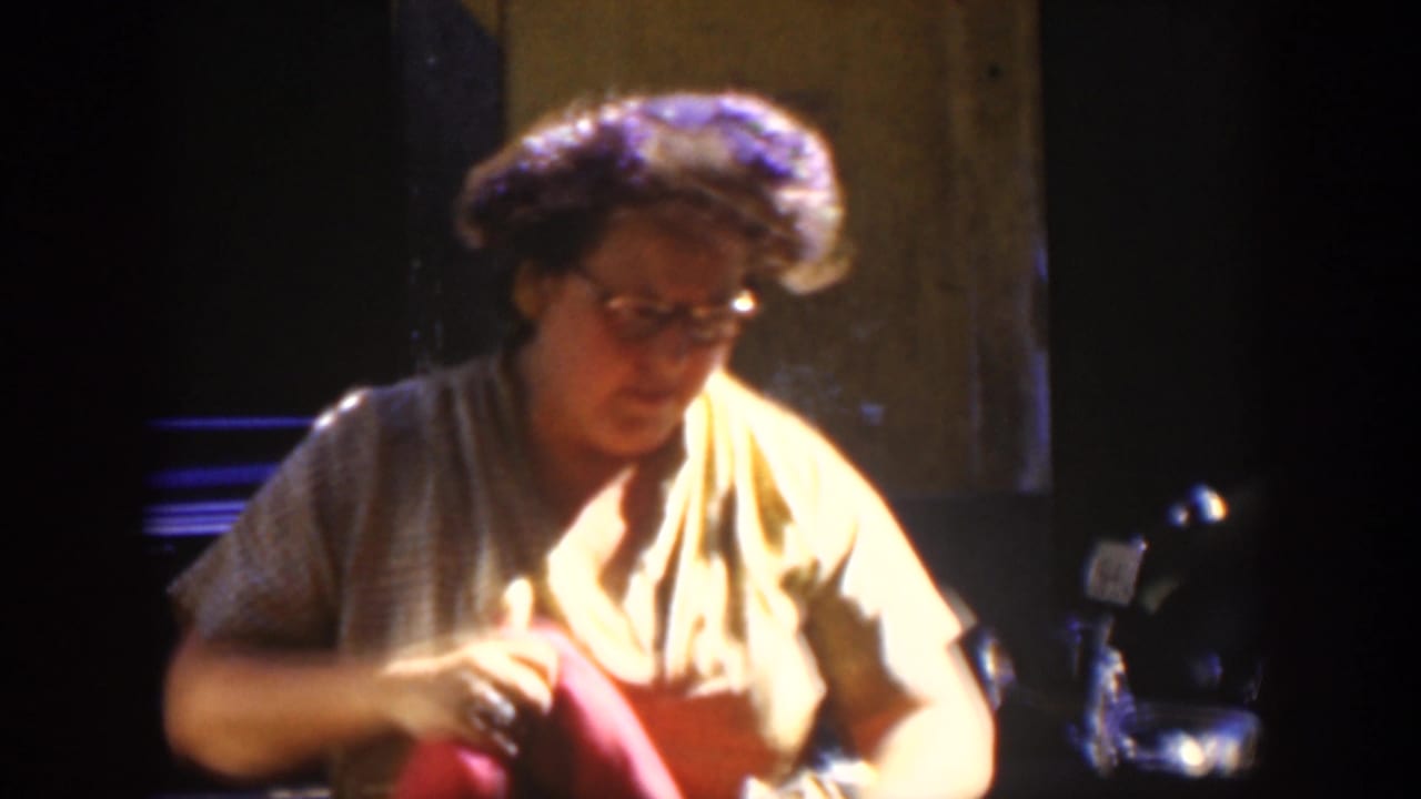 In 1951 Cuba footage, a woman with glasses sits in warm interior light while handling a red cloth.