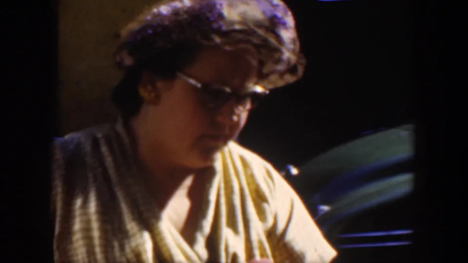 A close 1951 Cuba home-movie view shows a woman with glasses leaning forward in a softly lit interior.