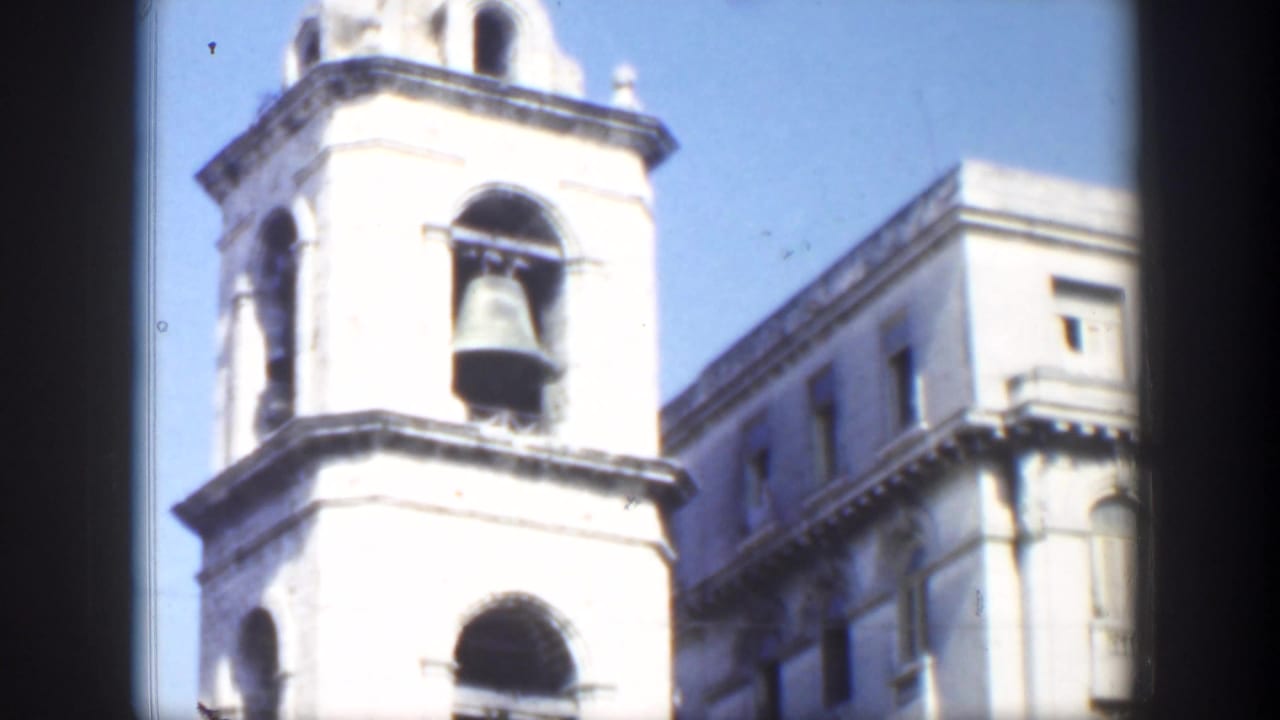 Sunlit stone bell tower with arched openings beside a taller building.