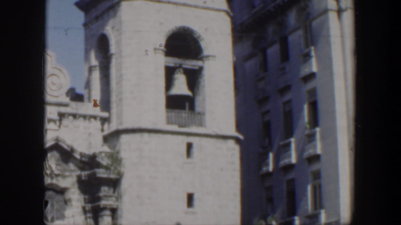 A 1951 Cuba home-movie frame shows part of an ornate stone church facade with a prominent bell tower under bright daylight.