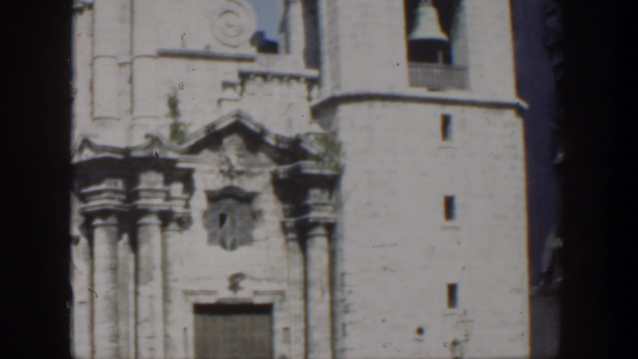 A Cuba 1951 frame shows the church's carved entrance and tall bell tower, with dark film borders and adjacent urban buildings visible.